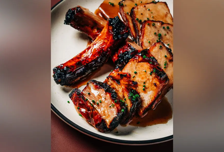 A wood-fired pork chop is sliced and covered with a house glaze.