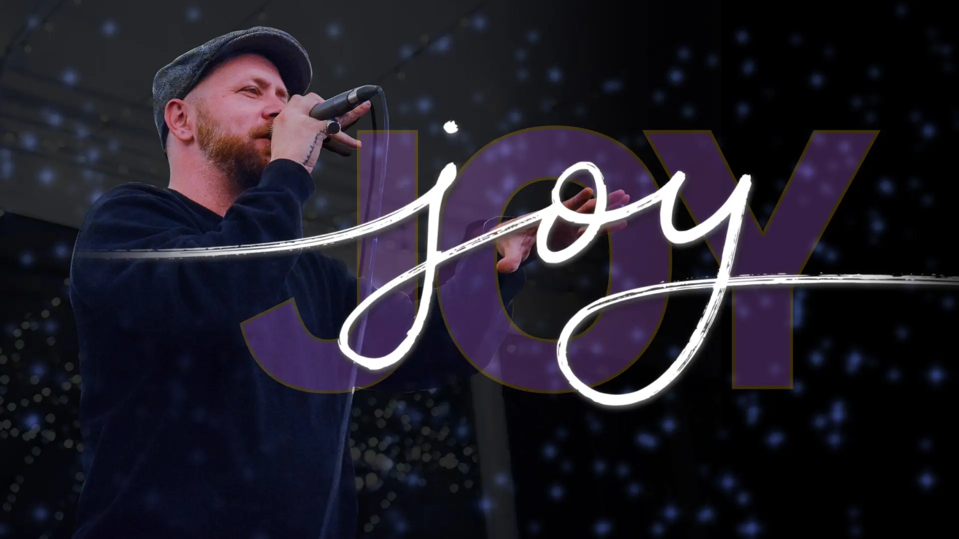 Poet speaks into microphone with stylized wording for the term "joy" beside him