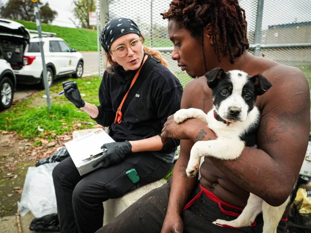 A woman talks to a homeless man holding a dog