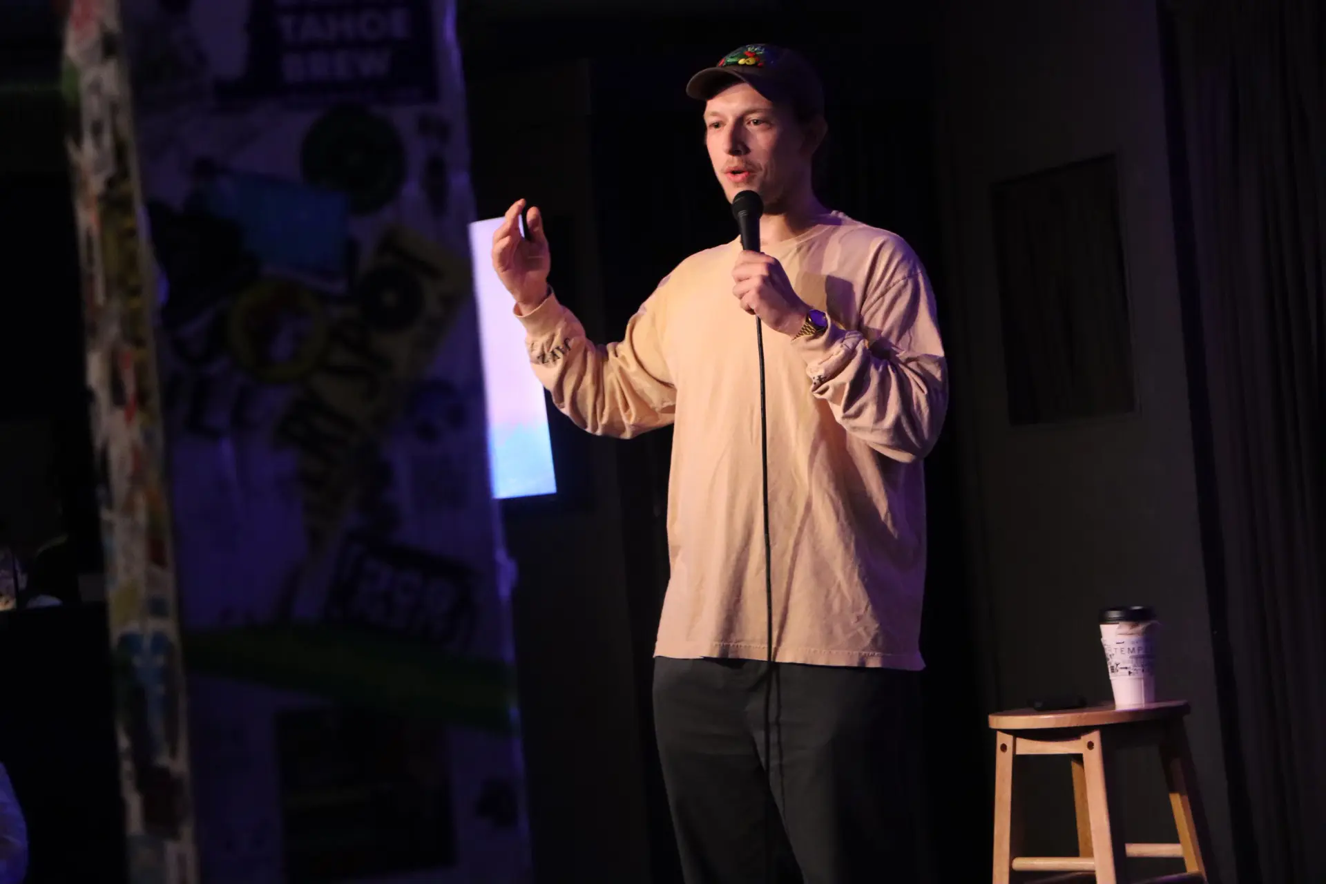 man in tan shirt holds mic at a comedy night set