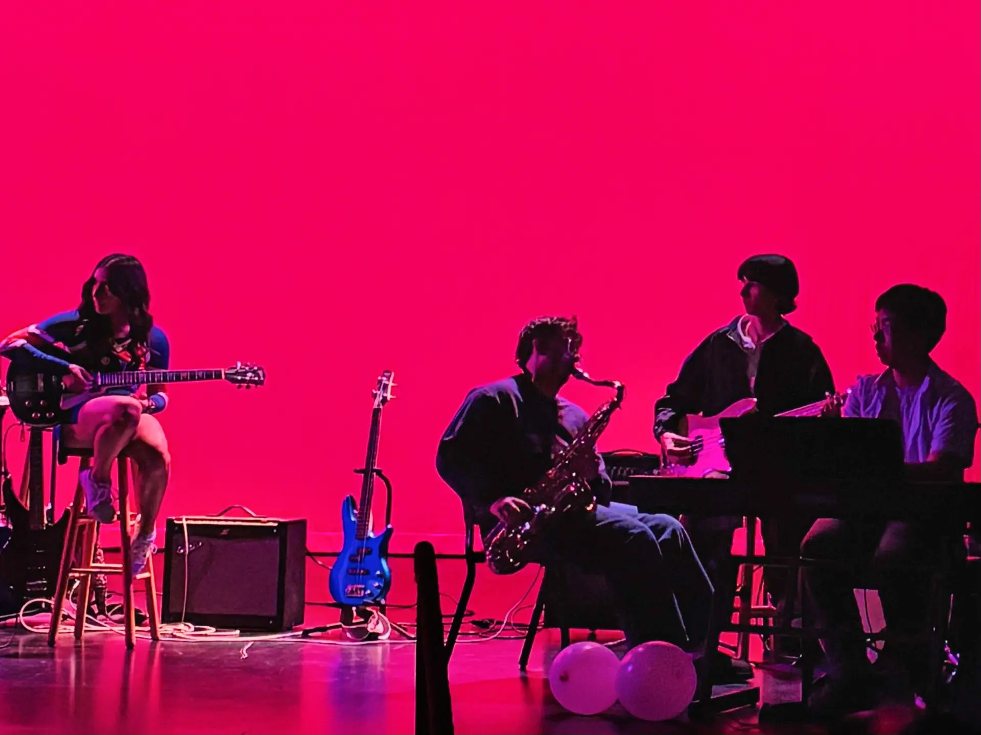 teenagers play instruments in front of a red background.