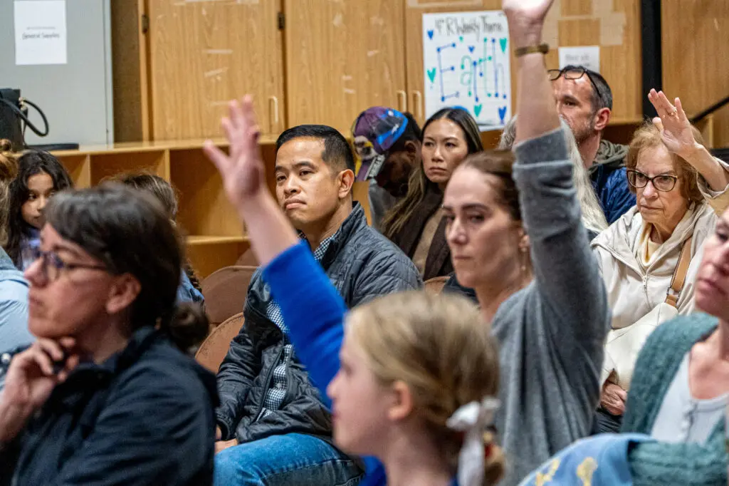 Parents raise hands at a meeting