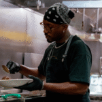 Chef standing in kitchen holding spoon, preparing food