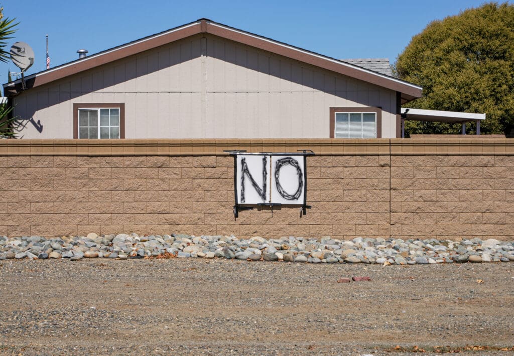 Large poster with the word "NO" taped onto a brick wall with black duct tape, as seen near the North Natomas tiny home site.