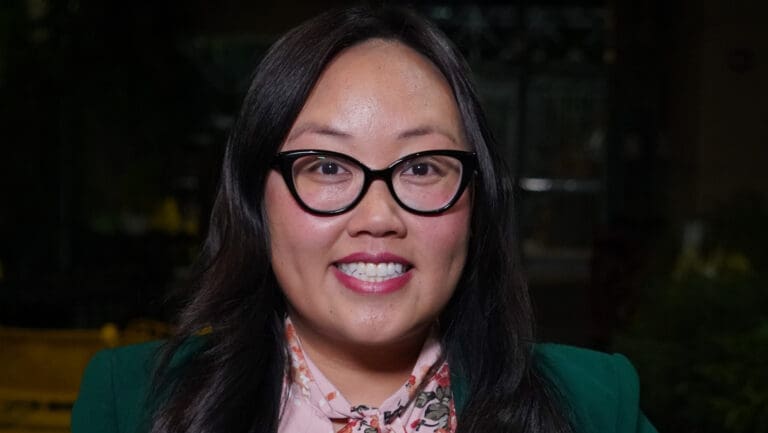Sacramento City Councilmember Mai Vang smiles in a green jacket and pink dress