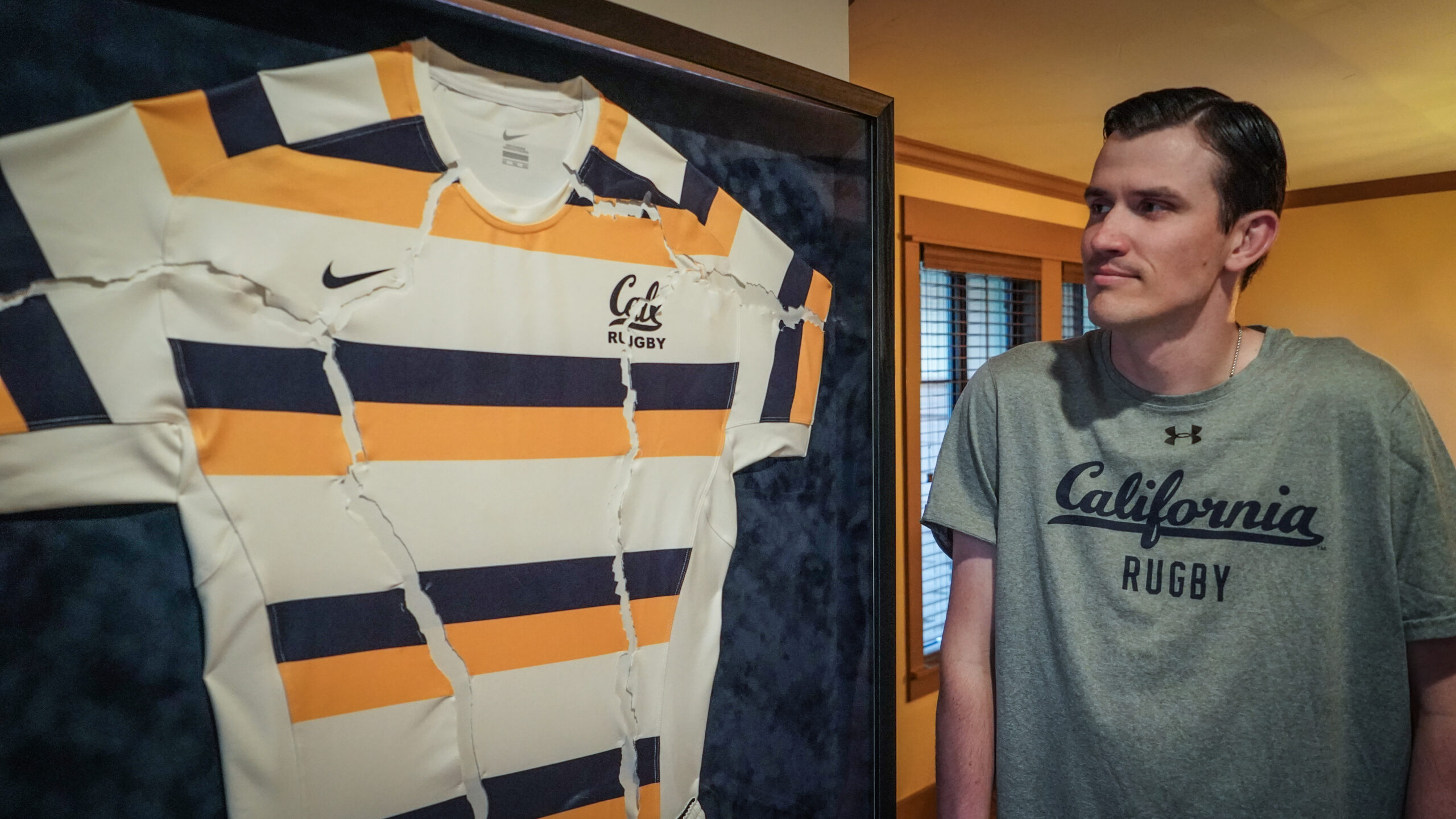 Man wearing California Rugby shirt glances sideways at a ripped jersey that is framed.
