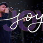 Poet speaks into microphone with stylized wording for the term "joy" beside him