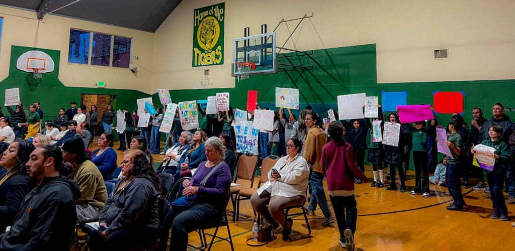 Students and parents in a gym holding signs