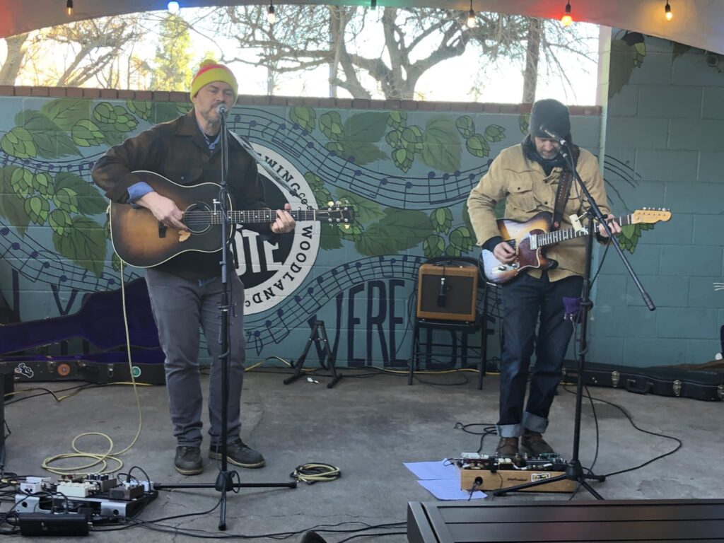 Two men play guitars with blue and green backdrop with music notes