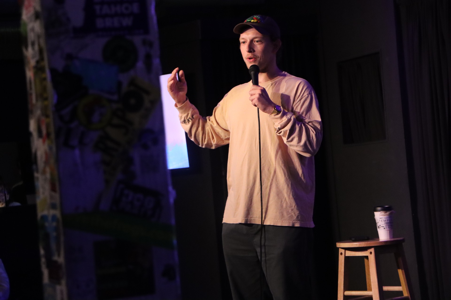 man in tan shirt holds mic at a comedy night set