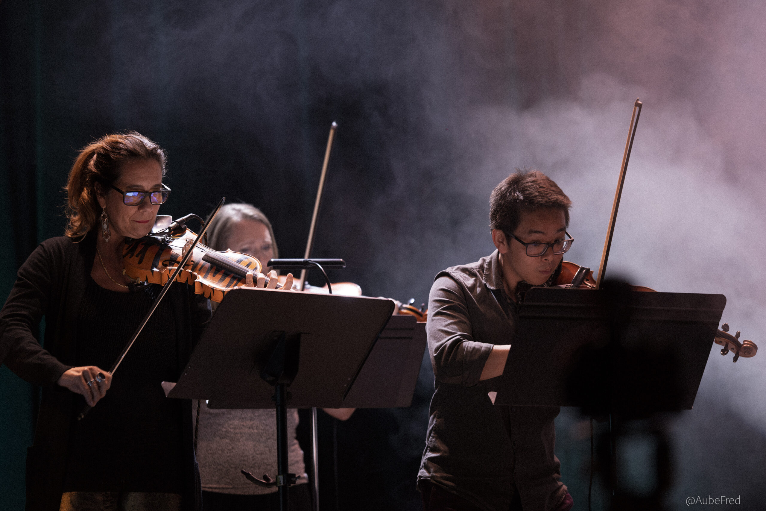 Three people play violin on a stage