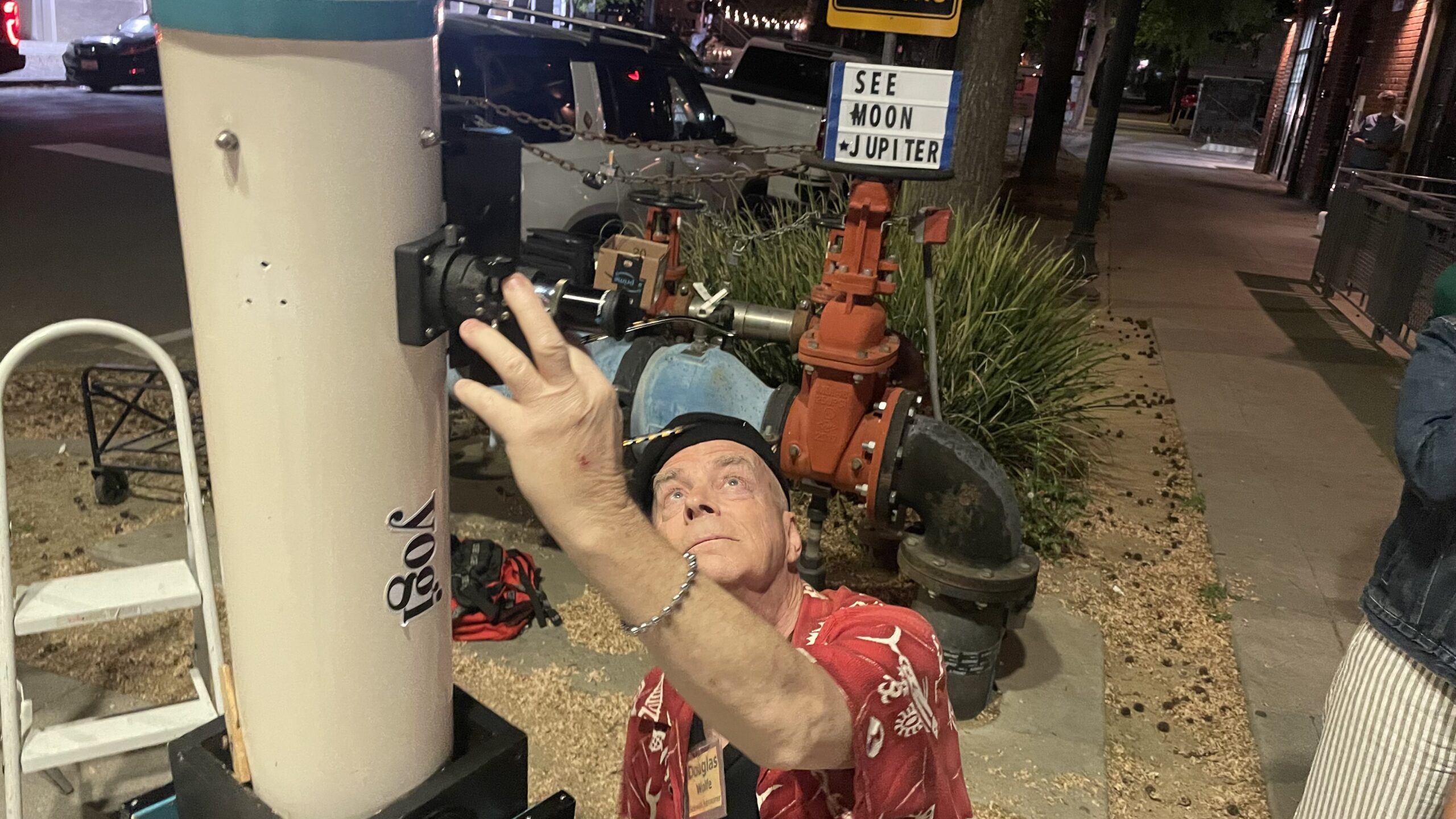 Man on sidewalk points large telescope toward the sky.