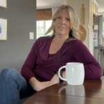 Woman sits at table with a coffee mug.