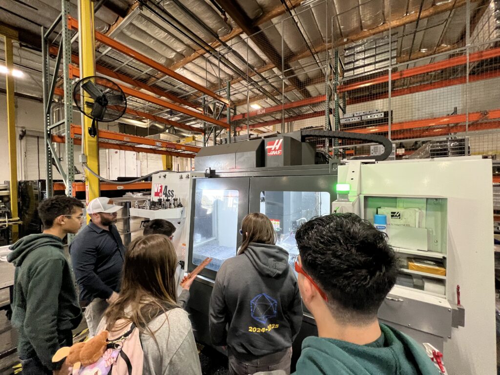 Students watch a CNC machine cut a stainless steel part at Roseville Precision Inc. in Rocklin.