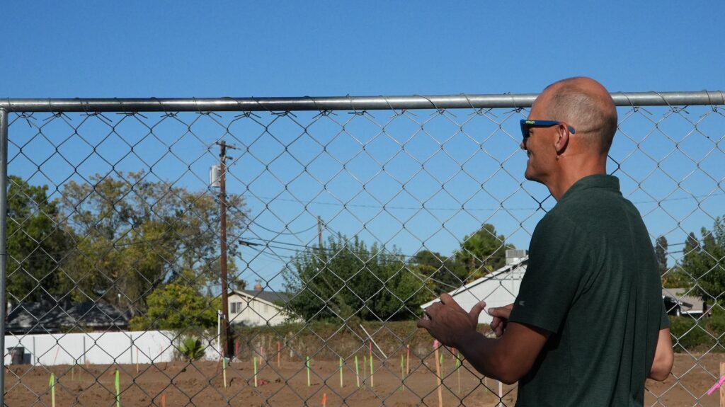 Man in green shirt stands outside fence