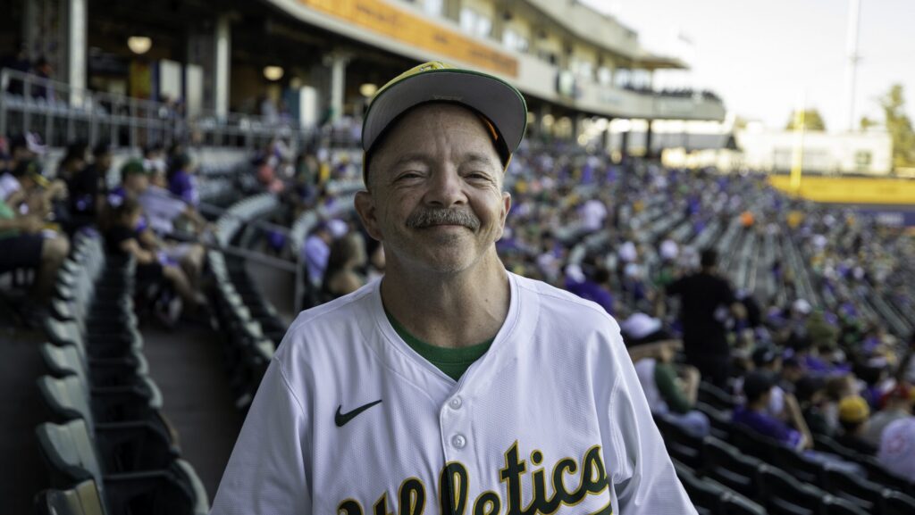 Man wearing baseball fan jersey smiles at the camera.
