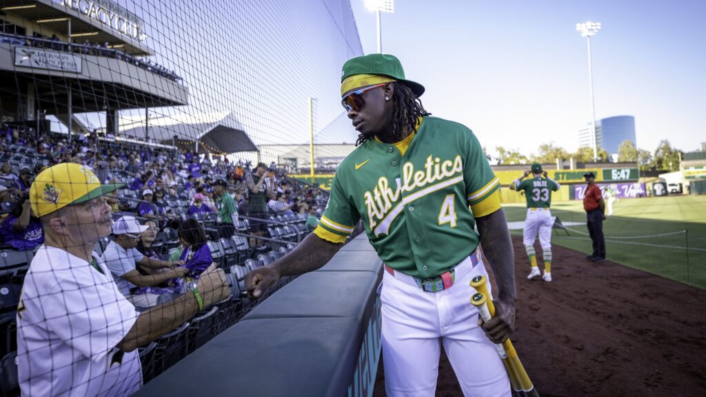 Baseball player for the A's gives fist bump to man in the stands.