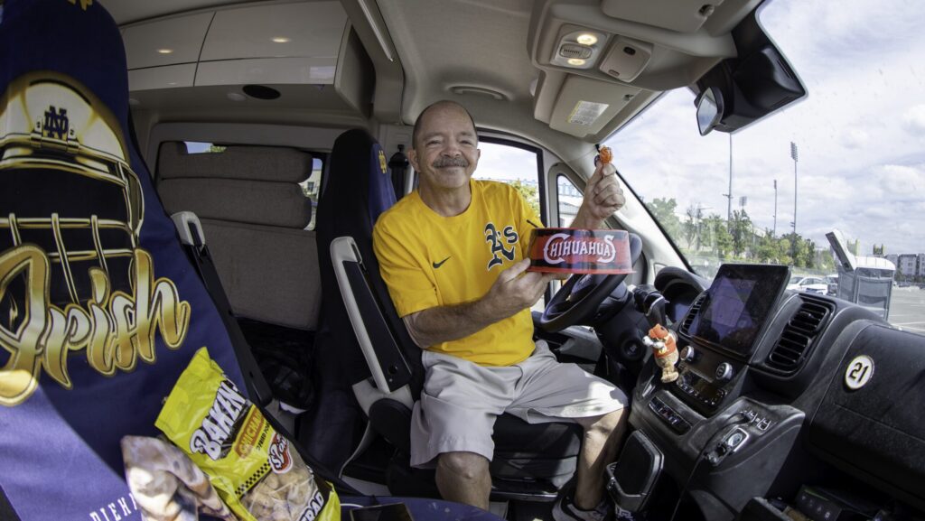 Man sits in the driver's seat in his RV and holds up sports memorabilia.