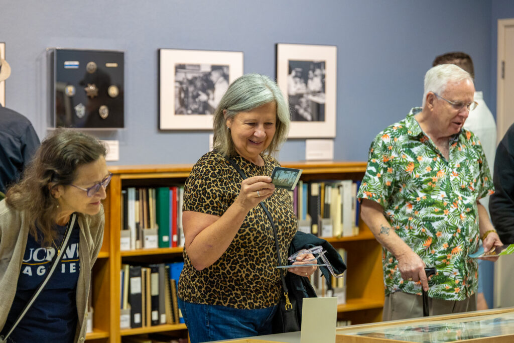 Three people stand in a line and look at items.