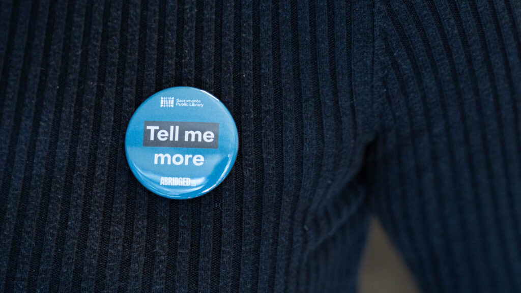 blue button that says tell me more on a black shirt